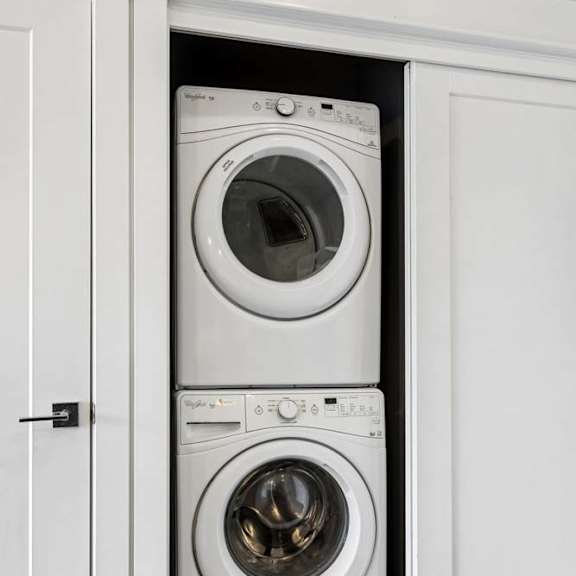 Thumbnail 39 of 46 Stacked washer and dryer fit neatly into a recessed apartment laundry closet with white sliding doors and trim.