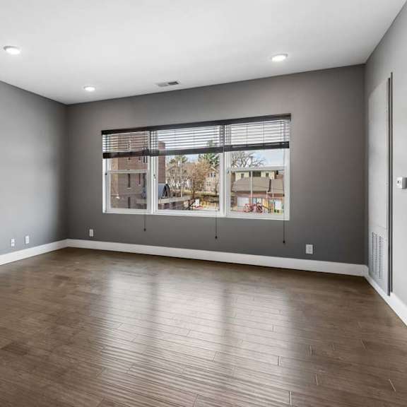 Thumbnail 40 of 46 Expansive apartment living room features wood-look flooring, gray walls, and a broad window overlooking the surrounding community.