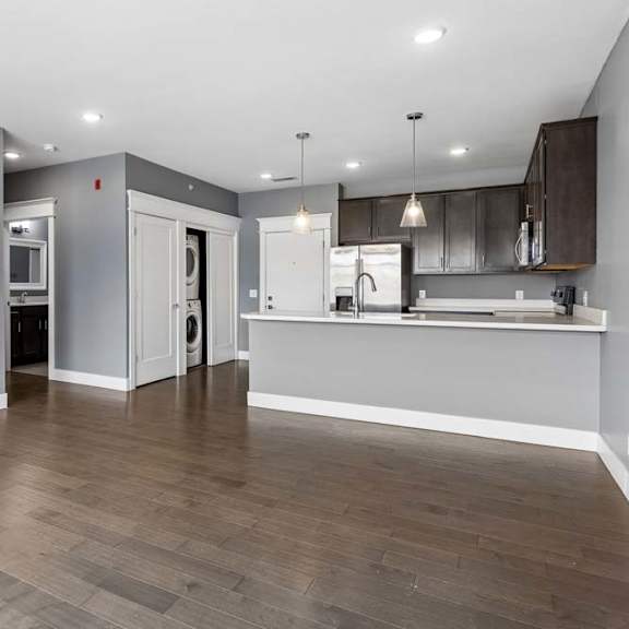 Thumbnail 41 of 46 Open apartment living area leads into a kitchen with dark cabinetry, a breakfast bar, pendant lighting, and nearby in-home laundry.