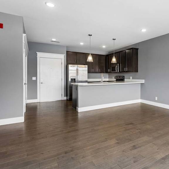 Thumbnail 42 of 46 Generous living area with wood-look flooring opens to a dark-cabinet kitchen, breakfast bar, and stainless steel appliances.