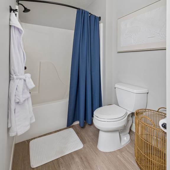 Thumbnail 34 of 39 Apartment bathroom with blue shower curtain, wood-style flooring, and open shelving.