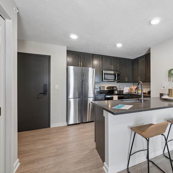 Thumbnail 25 of 39 Apartment kitchen with island barstool seating, stainless steel appliances, and dark cabinetry.