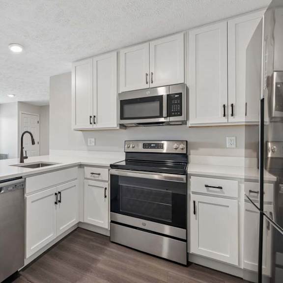 Thumbnail 23 of 36 Apartment kitchen with white cabinetry, stainless steel appliances, and peninsula seating.