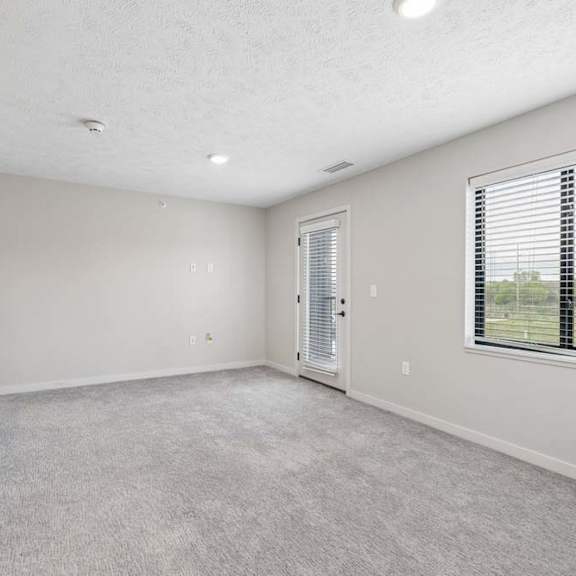 Thumbnail 26 of 36 Apartment living area with neutral carpeting, large window, and glass door leading to a private balcony.