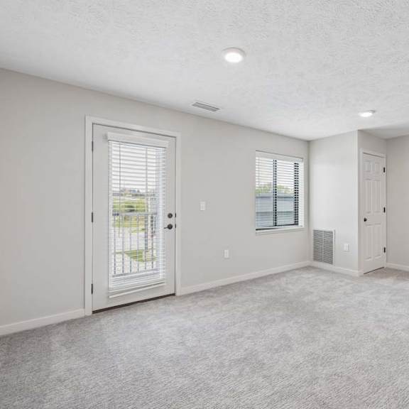 Thumbnail 25 of 36 Open apartment living area with neutral carpeting, large window, and patio door with blinds.