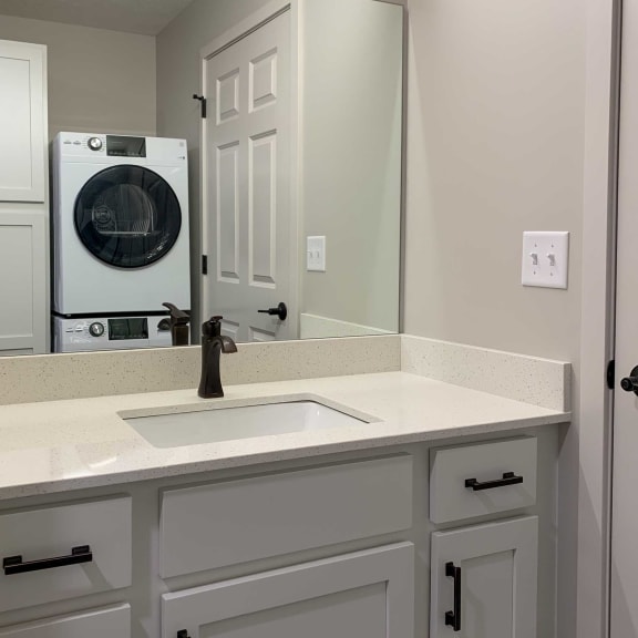 Thumbnail 12 of 15 a bathroom with white cabinets and stackable washer and dryer