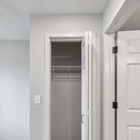 Thumbnail 39 of 52 Walk-in apartment closet with built-in shelving, hanging rods, and neutral finishes, accessible through a white paneled door.