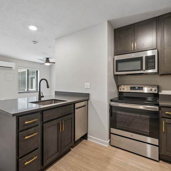 Thumbnail 34 of 52 Modern apartment kitchen with dark cabinetry, stainless steel appliances, a center island with storage, and an open layout connected to the living area.