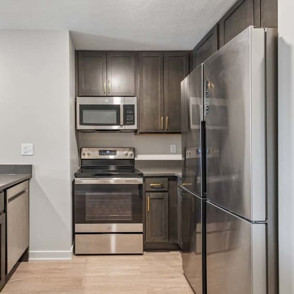 Thumbnail 35 of 52 Apartment kitchen with dark cabinetry, stainless steel refrigerator, microwave, and oven, plus durable countertops and a functional galley-style layout.