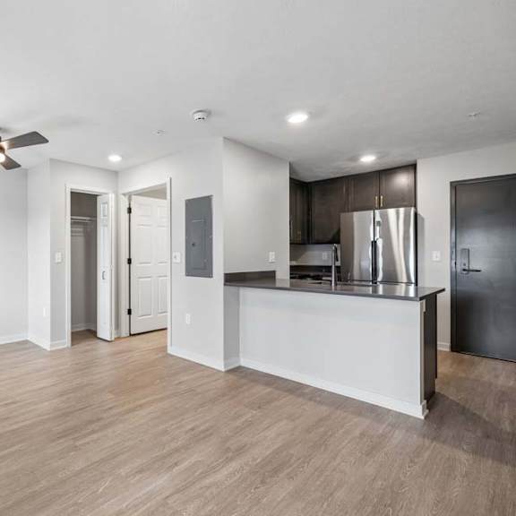 Thumbnail 36 of 52 Open-concept apartment living area with wood-style flooring, a ceiling fan, and a kitchen featuring dark cabinetry, stainless steel appliances, and a breakfast bar.