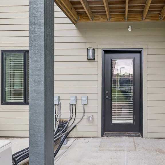 Thumbnail 42 of 52 Covered ground-floor apartment patio with a concrete surface, exterior wall lighting, and a glass-paneled door leading into the residence.