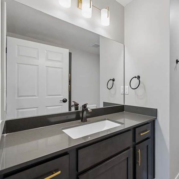 Thumbnail 49 of 52 Apartment bathroom with a single-sink vanity, dark cabinetry, a large mirror, and a tub-shower combination with a white surround and modern black fixtures.