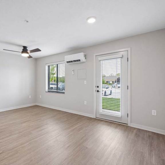 Thumbnail 48 of 52 Bright apartment living room with wood-style flooring, recessed lighting, a ceiling fan, a glass patio door, and a wall-mounted mini-split heating and cooling unit.