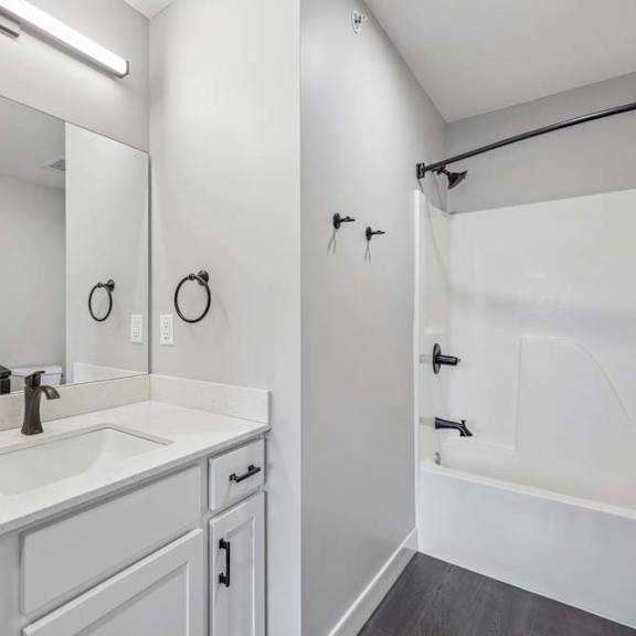 Thumbnail 31 of 52 Apartment bathroom with white vanity, black fixtures, and tub-shower combination with surround.
