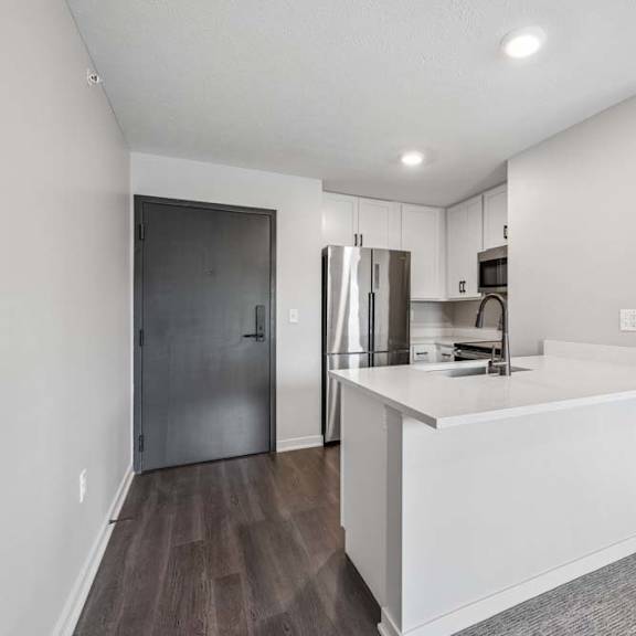 Thumbnail 27 of 52 Apartment kitchen with peninsula seating, stainless steel appliances, and dark wood-style flooring.