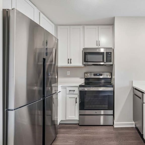 Thumbnail 25 of 52 Apartment kitchen with white cabinetry, stainless steel appliances, and oversized peninsula with built-in sink.