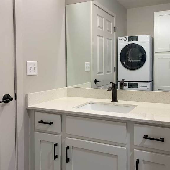 Thumbnail 24 of 25 a bathroom vanity sink with white cabinets and a stackable washer and dryer in the mirrors reflection
