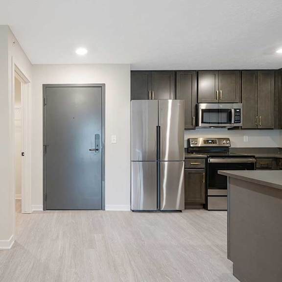 Thumbnail 16 of 30 The front door with partial view of the kitchen with dark cabinets and countertops