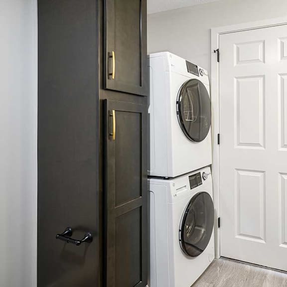 Thumbnail 17 of 25 a stacked washer and dryer next to a tall storage cabinet
