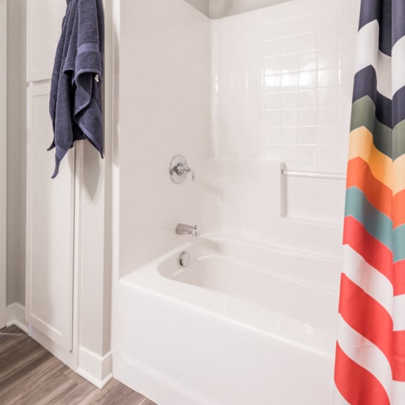 Thumbnail 13 of 18 white tub/shower with striped rainbow curtain and a blue towel handing next to it