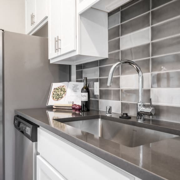 Thumbnail 7 of 18 wall of kitchen with dark gray and white backsplash, stainless steel sink and appliances, plus white cabinets