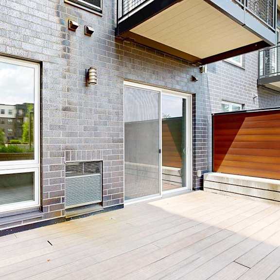 Thumbnail 16 of 31 A patio with wooden plank flooring, a large window to the bedroom, and a sliding glass door to the living room.