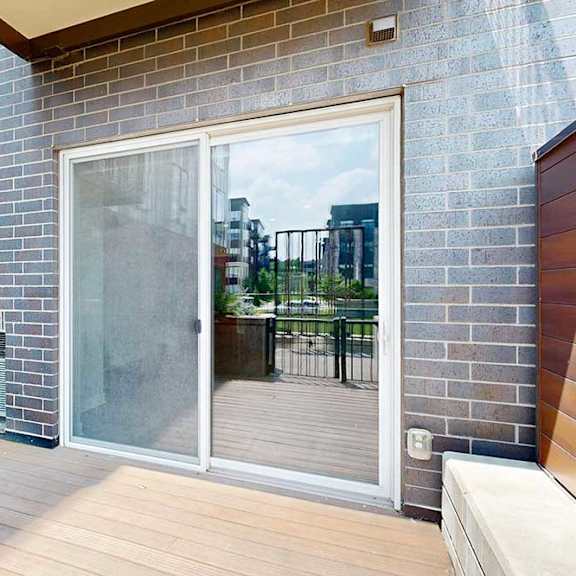 Thumbnail 13 of 31 A patio with wooden plank flooring, a large window to the bedroom, and a sliding glass door to the living room.