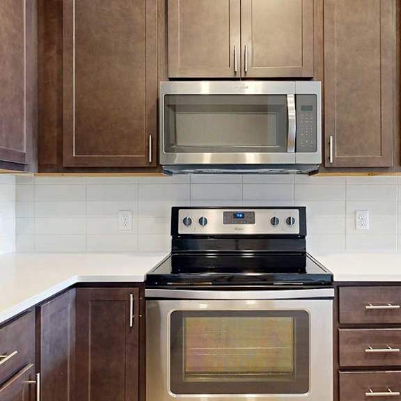 Thumbnail 9 of 31 A close up on a stainless steel range and microwave in a kitchen with dark wooden cabinets.