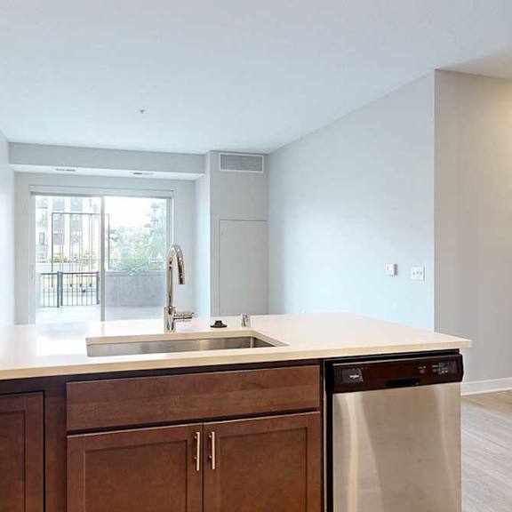 Thumbnail 10 of 31 A kitchen peninsula with dark wooden cabinets, quartz countertops, and stainless steel appliances, in front of a living room.