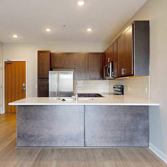 Thumbnail 6 of 31 A modern kitchen with wooden cabinets, quartz countertops, a tile backsplash, stainless steel appliances, and a peninsula.