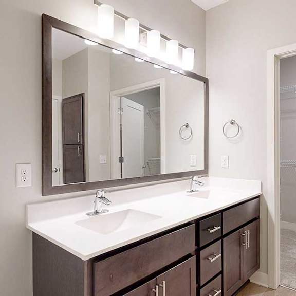 Thumbnail 17 of 22 A bathroom with a double sink marble vanity, oversized mirror, dark wooden cabinets, and a door open to walk-in closet.