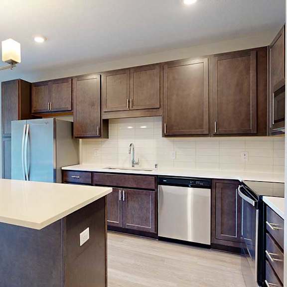 Thumbnail 6 of 22 A kitchen with dark wood cabinets, quartz countertops, a large island, stainless steel appliances, and a designer backsplash.