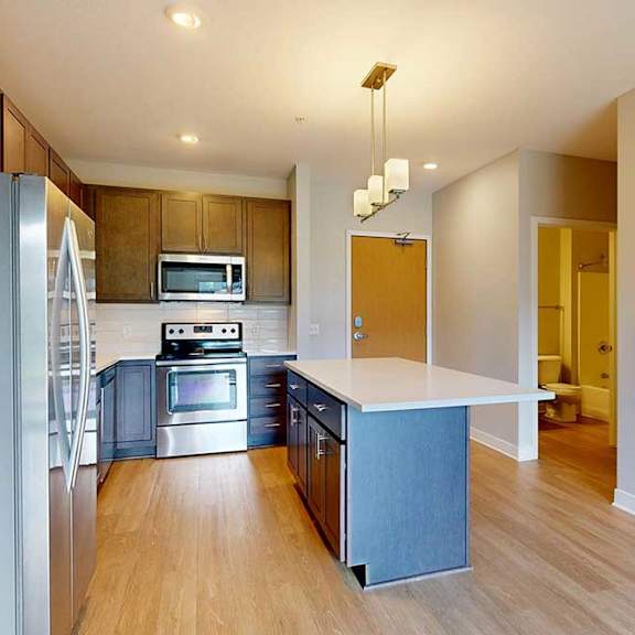 Thumbnail 4 of 22 A kitchen with dark wood cabinets, quartz countertops, a large island, stainless steel appliances, and a designer backsplash.