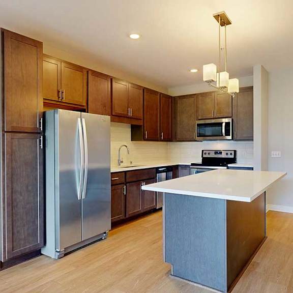 Thumbnail 5 of 22 A kitchen with dark wood cabinets, quartz countertops, a large island, stainless steel appliances, and a designer backsplash.