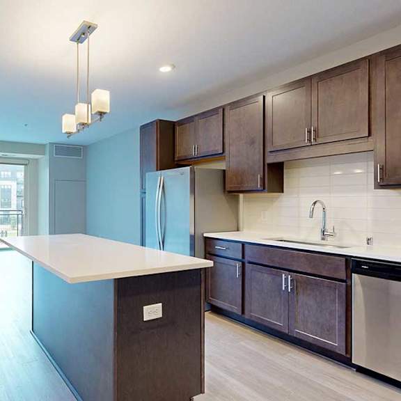 Thumbnail 10 of 22 A kitchen with dark wooden cabinets and a large island, in front of a spacious living room.