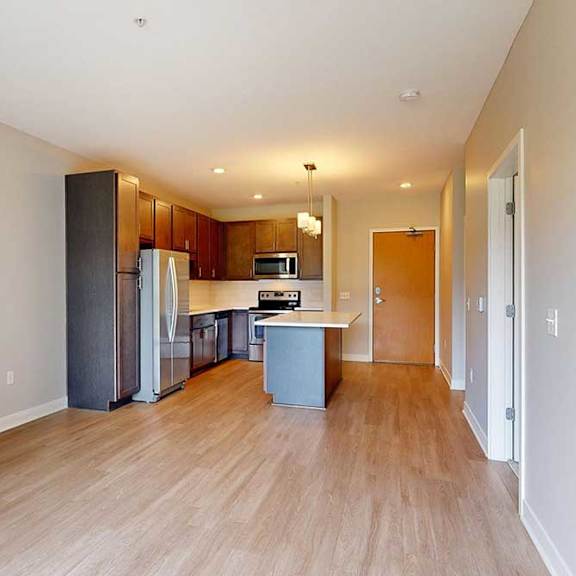 Thumbnail 14 of 22 A living room with hardwood-style flooring and kitchen with dark wooden cabinets.