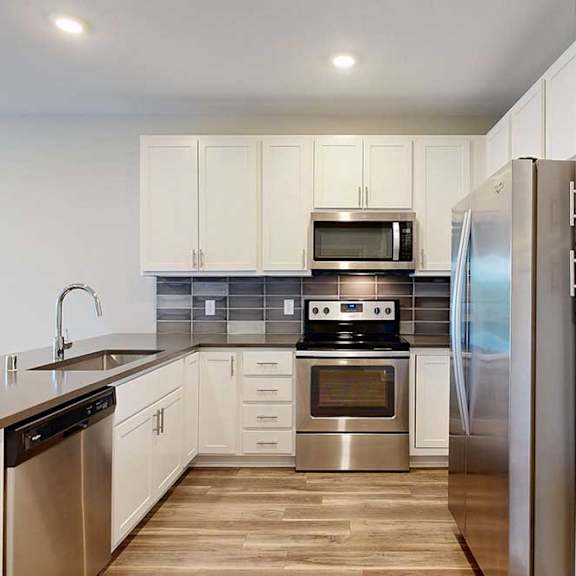 Thumbnail 6 of 25 A kitchen with white wooded cabinets, quartz countertops, a peninsula, stainless steel appliances, and a designer backsplash.