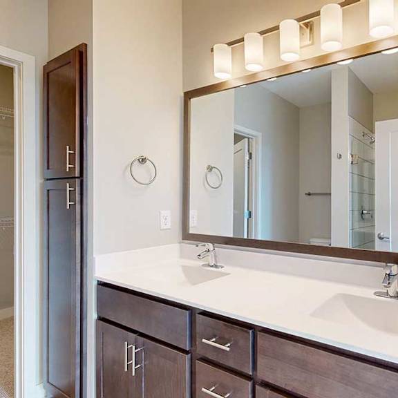 Thumbnail 16 of 27 A bathroom with a double sink marble vanity, oversized mirror, and dark wooden cabinets.
