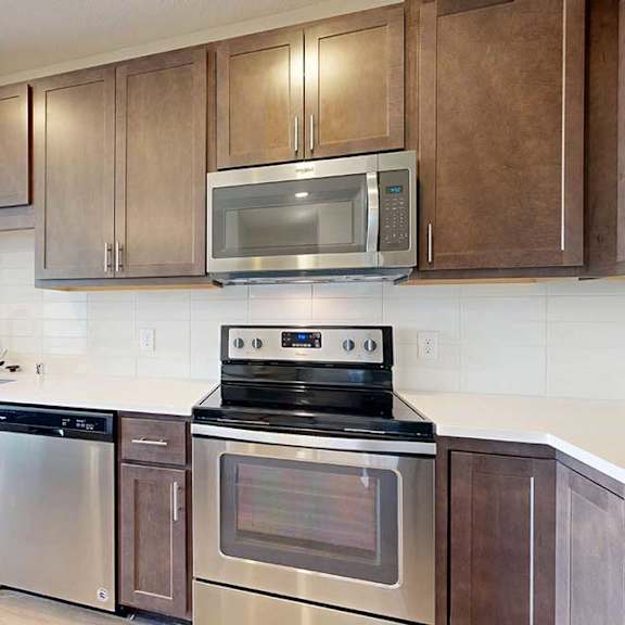 Thumbnail 7 of 27 A kitchen with dark wood cabinets, quartz countertops, a large island, stainless steel appliances, and a designer backsplash.