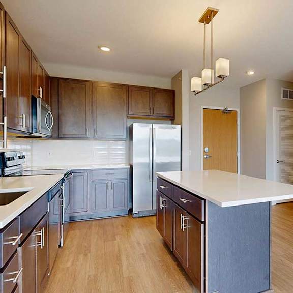 Thumbnail 4 of 27 A kitchen with dark wood cabinets, quartz countertops, a large island, stainless steel appliances, and a designer backsplash.