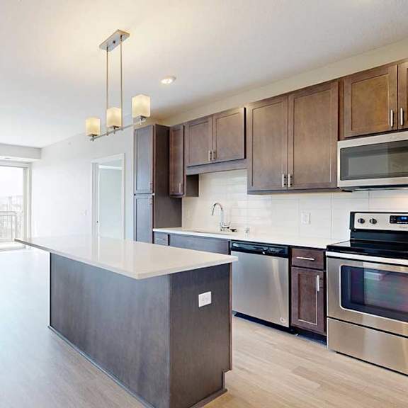 Thumbnail 8 of 27 A kitchen with dark wood cabinets and stainless steel appliances, open to a living area with hardwood-style flooring.