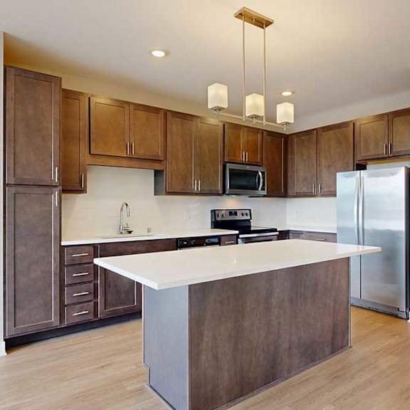 Thumbnail 5 of 27 A kitchen with dark wood cabinets, quartz countertops, a large island, stainless steel appliances, and a designer backsplash.