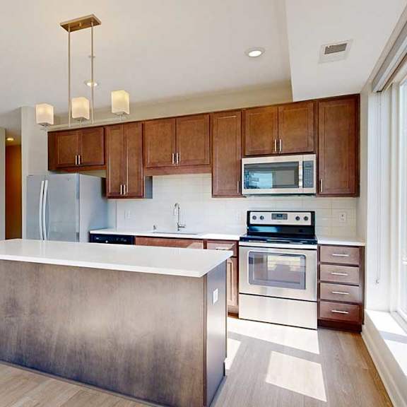 Thumbnail 14 of 27 A kitchen with dark wood cabinets, quartz countertops, a large island, stainless steel appliances, and a designer backsplash.
