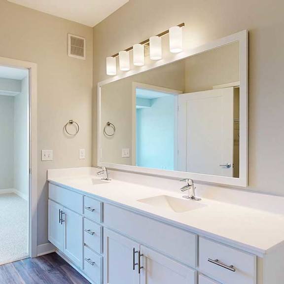 Thumbnail 18 of 29 A bathroom with a double sink marble vanity, oversized mirror, white wooden cabinets, and a door open to a bedroom.
