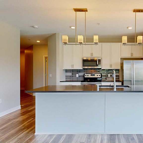 Thumbnail 6 of 29 A kitchen with white wooden cabinets, quartz countertops, a large island, stainless steel appliances, and a designer backsplash.