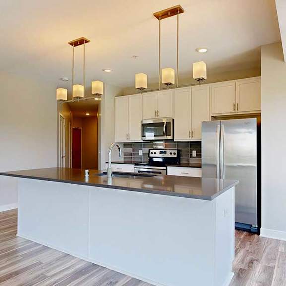 Thumbnail 4 of 29 A kitchen with white wooden cabinets, quartz countertops, a large island, stainless steel appliances, and a designer backsplash.