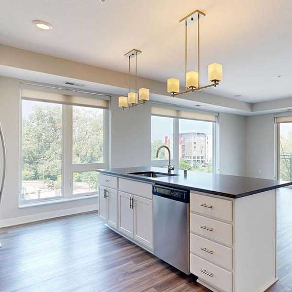 Thumbnail 10 of 29 A kitchen island in front of a living room with floor-to-ceiling windows, hardwood-style flooring, and a sliding glass door to a balcony.