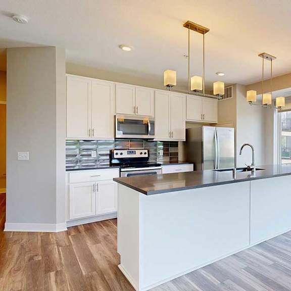 Thumbnail 7 of 29 A kitchen with white wooden cabinets, quartz countertops, a large island, stainless steel appliances, and a designer backsplash.