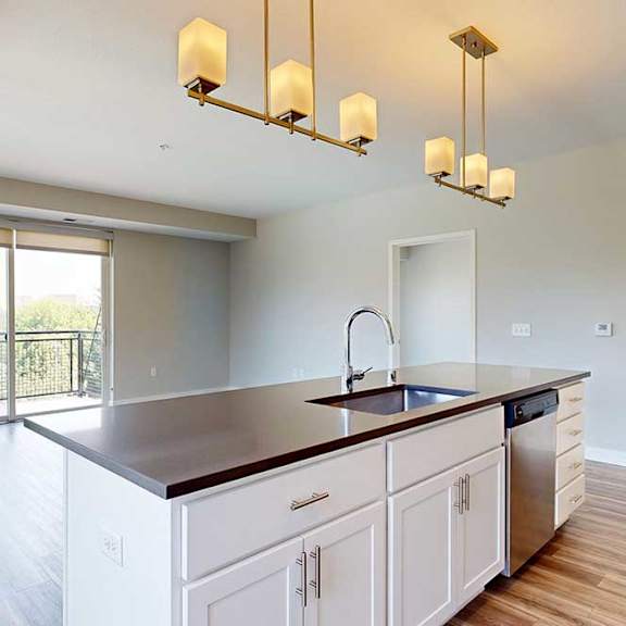 Thumbnail 9 of 29 A kitchen island in front of a living area with hardwood-style flooring and a sliding glass door to a balcony.