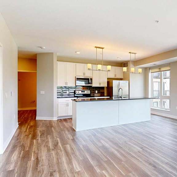 Thumbnail 8 of 29 A living room with hardwood-style flooring and kitchen with white wooden cabinets.